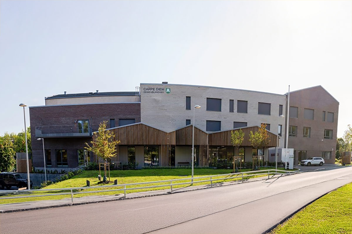 Fasaden til Carpe Diem Demenslandsby med bilvei i forkant