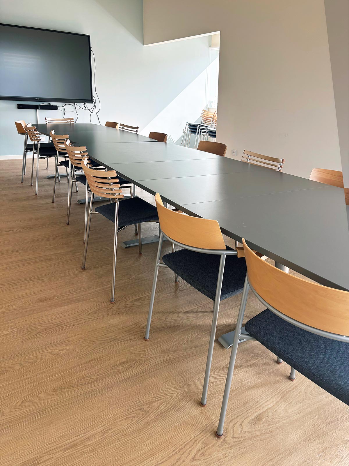 møterom med et langt møtebord med stoler. i enden henger en tv på veggen