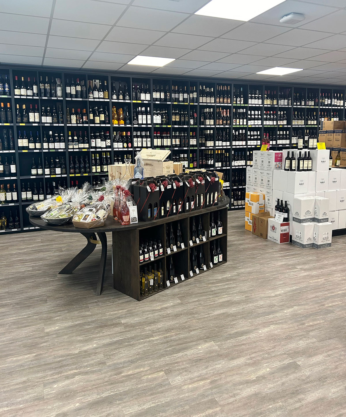 butikk med hyller langs hele bakveggen med vin. I forgrunnen ser man et butikktorg og til høyre noen vinesker med løse  flasker stående oppå