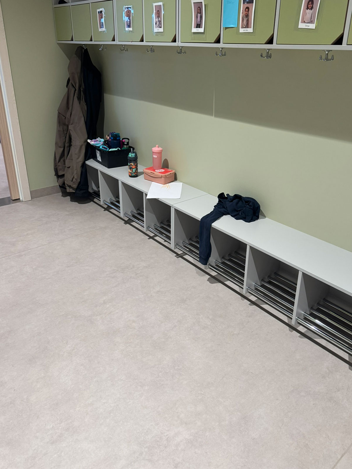 lav benk i gangen eller skifterommet på en barnehage. grønn vegg med skap hengene høyt