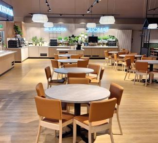 en lys og fin kafeteria i Finland med runde bord og stoler stående midt på gulvet. Til venstre er disken og til høyre er andre spisegrupper