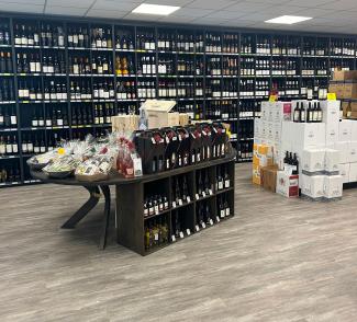 butikk med hyller langs hele bakveggen med vin. I forgrunnen ser man et butikktorg og til høyre noen vinesker med løse  flasker stående oppå