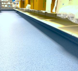 Lagerrom med hyller, esker og lyst blått gulvbelegg med oppbrett langs veggen.