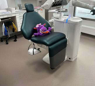 Tannlegebehandlingsrom med grønn behandlingsstol, teknisk utstyr og lyst, slitesterkt gulv med diskret prikkmønster.