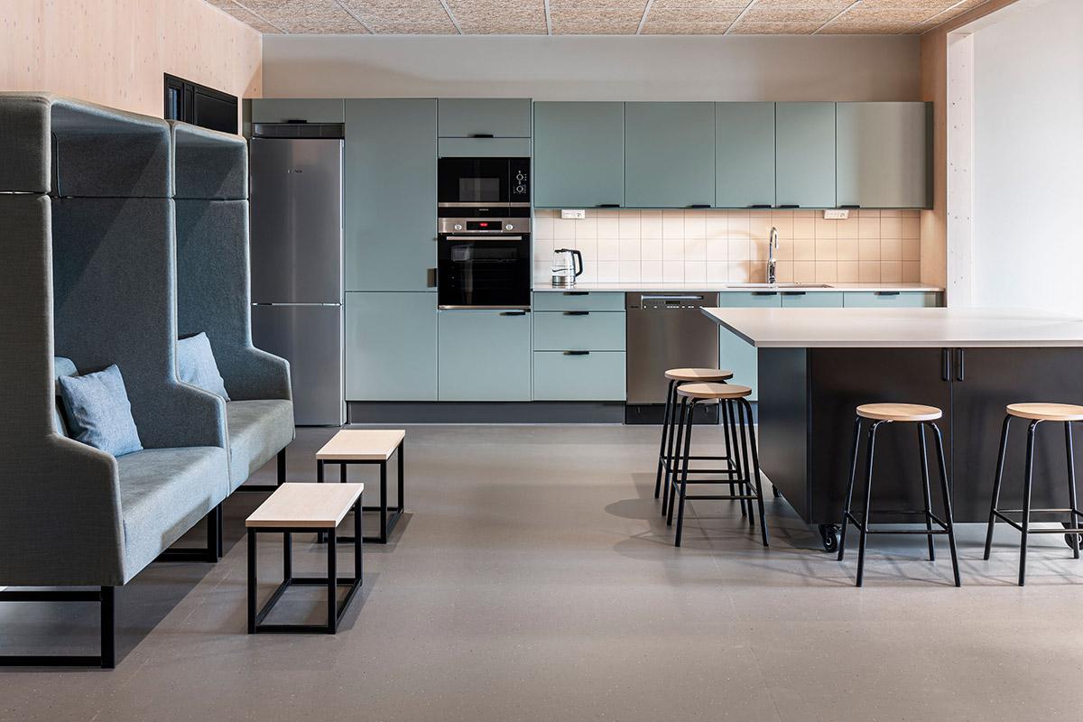 kjøkken/spiserom på skole med sittegrupper utformet som en boks til venstre og kjøkkenøy med stoler til hlyre