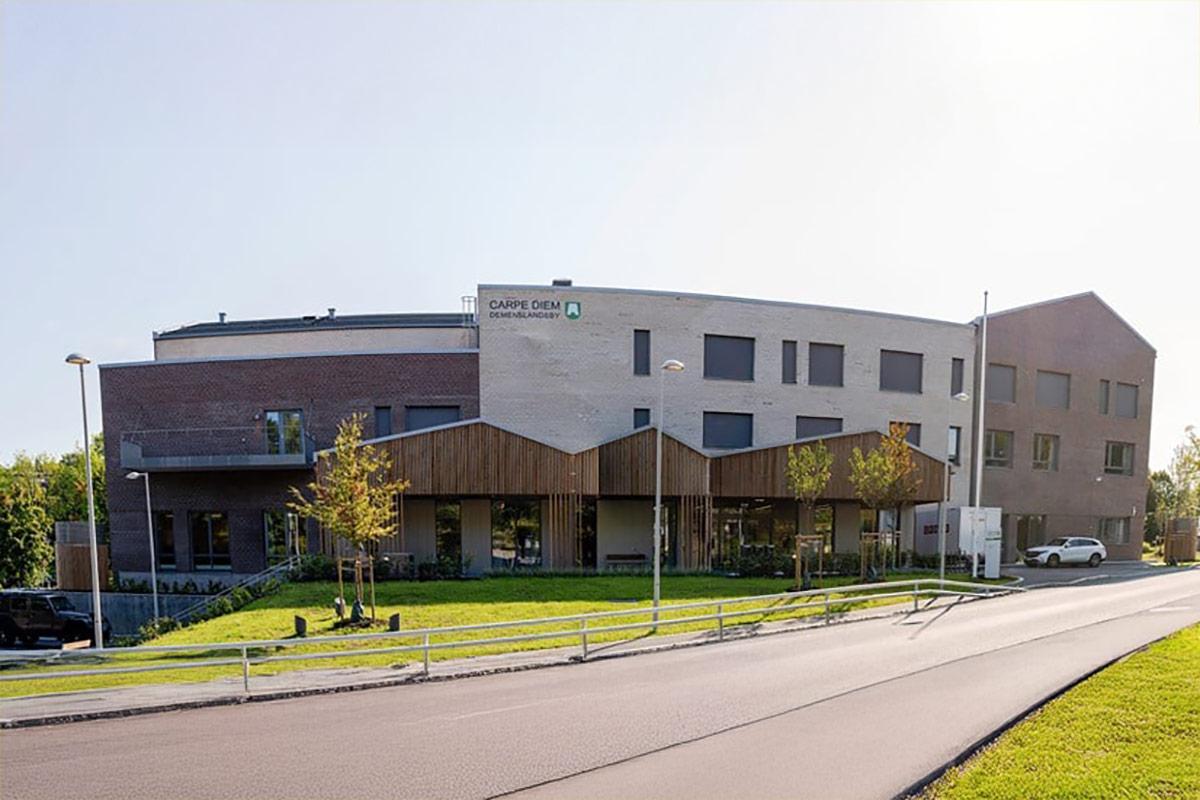 Fasaden til Carpe Diem Demenslandsby med bilvei i forkant