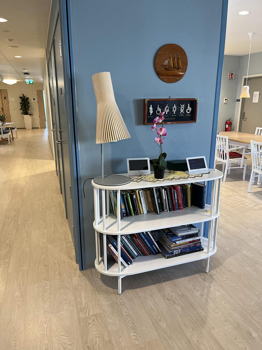 kort vegg malt i blått med en liten hylle og lampe foran. Til høyre kan man se inn på kjøkkenet og til venstre kan man se innover i gangen