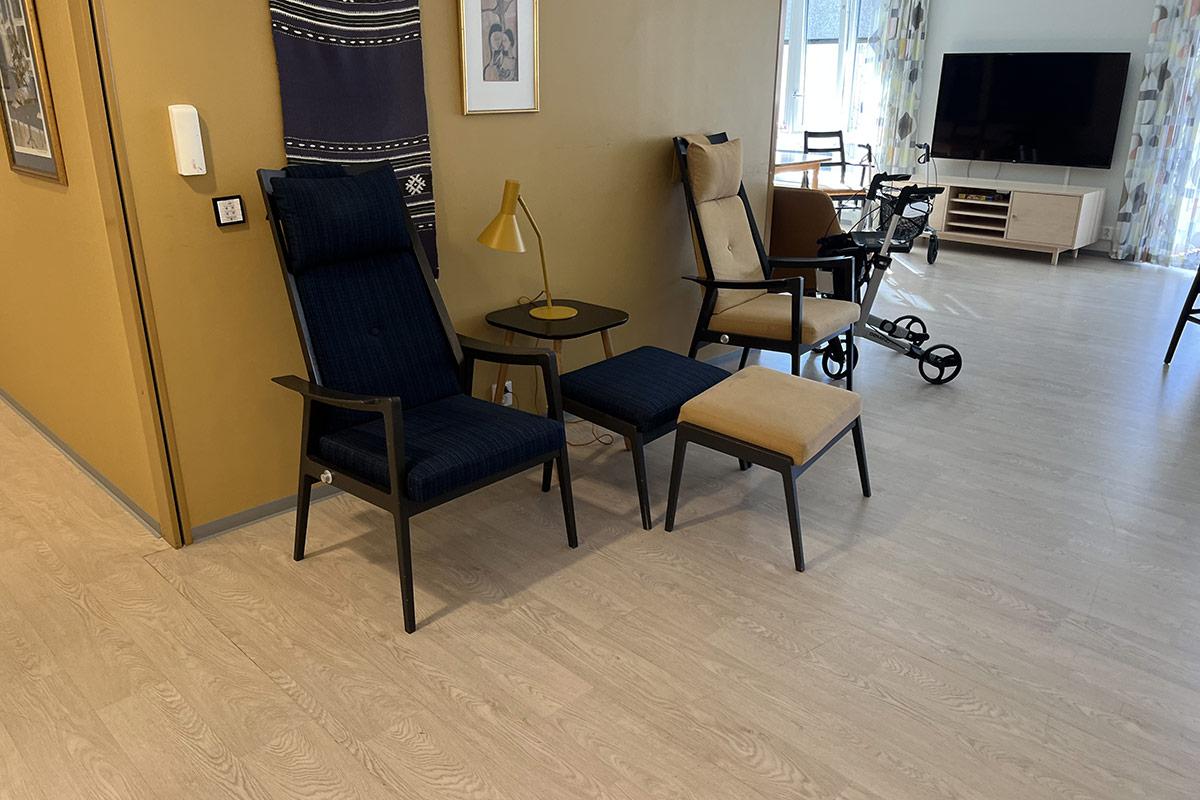 sittegruppe foran en sennepsgul vegg. I bakgrunnen ser man en tv på en tv-benk