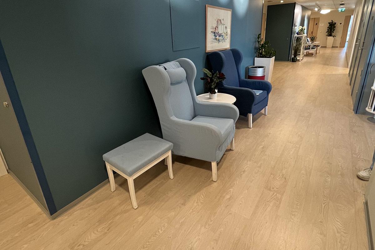 sittegruppe med to lenestoler og et bord stående inntill en blå vegg i gangen på Carpe Diem Demenslandsby
