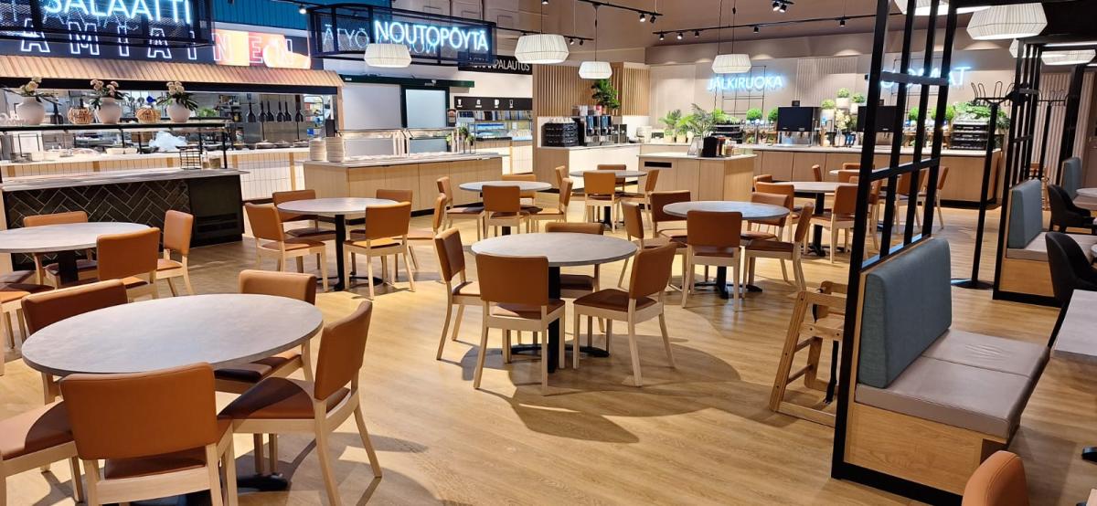 en lys og fin kafeteria i Finland med runde bord og stoler stående midt på gulvet. Til venstre er disken og til høyre er andre spisegrupper