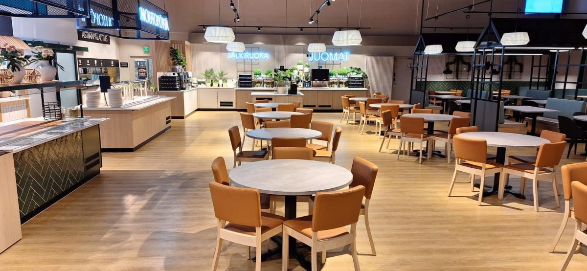 en lys og fin kafeteria i Finland med runde bord og stoler stående midt på gulvet. Til venstre er disken og til høyre er andre spisegrupper