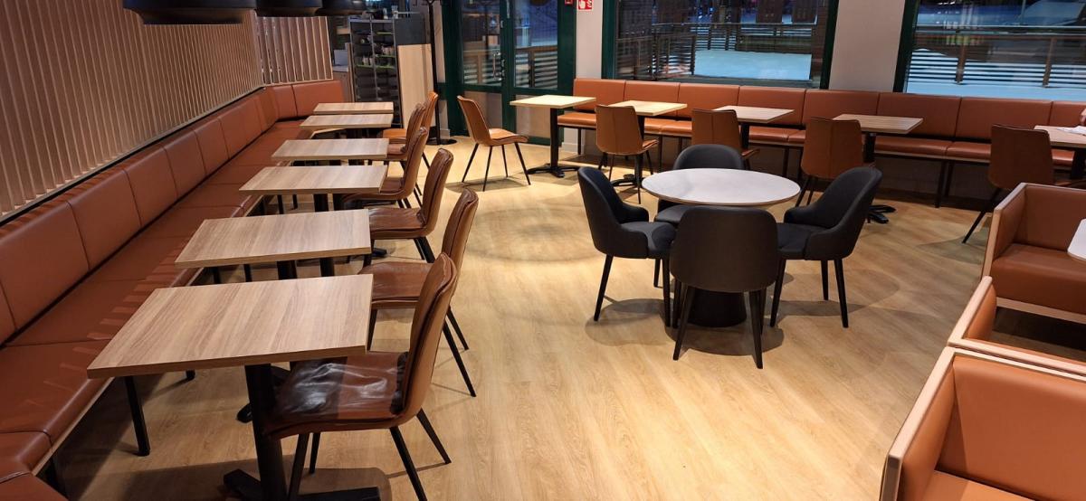 Spisegrupper i en kafeteria i Finland. Midt på gulvet står et rundt bord med stoler. Til venstre småbord med stol og lang sofa