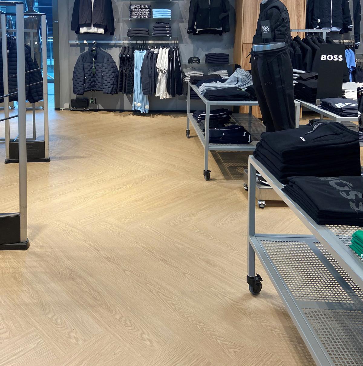 i en klesbutikk med et nytt gulv, bord med klær til høyre og hyller med klær i bakgrunnen