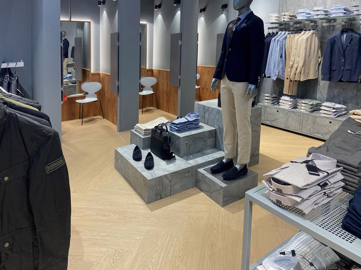 en prøvedukke midt på gulvet i en klesbutikk. Hyller med klær i bakgrunnen til høyre og tre prøverom i bakgrunnen til venstre