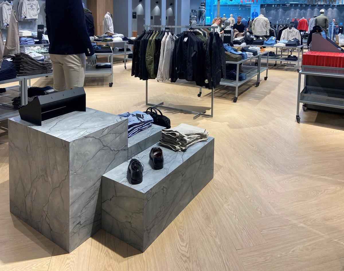 imiterte steinblokker med sko og klær liggene oppå i en klesbutikk. I bakgrunnen er det flere hyller og stativ med klær