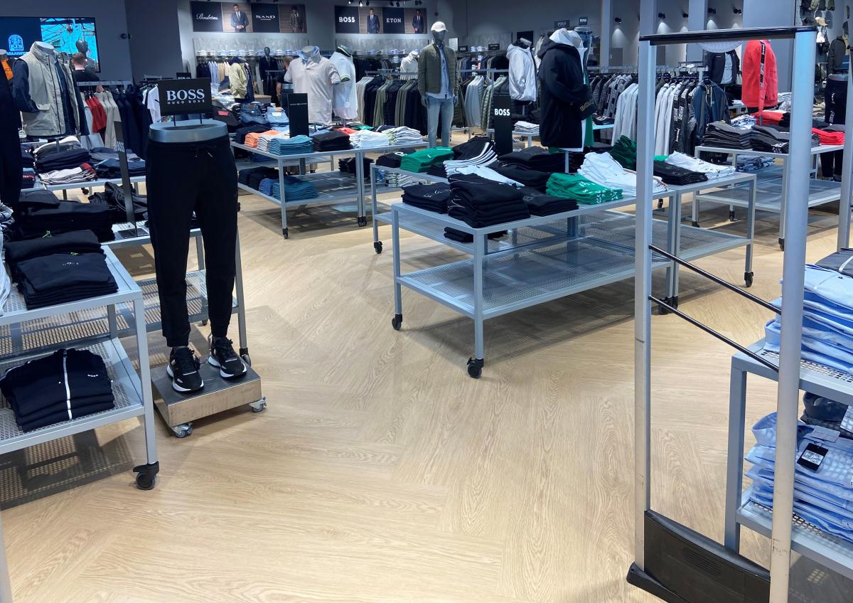 klesbutikk med mange bord og stativ med klær. På gulvet står det et par ben fra en utstillingsdukke med bukser fra Boss