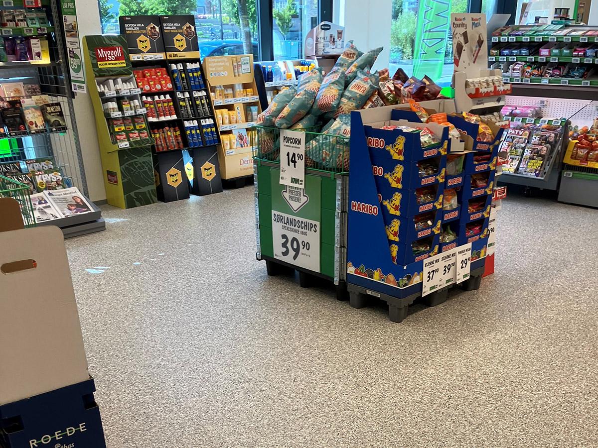 et frittstående varetorg i en kiwi butikk, med hyller i bakgrunnen til venstre og kasse i bakgrunnen til høyre