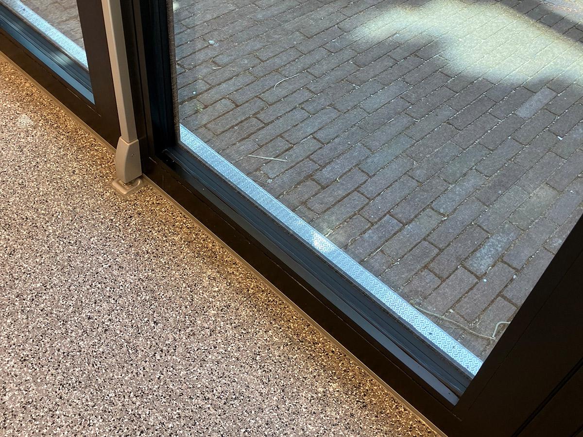 nærbilde av en glassdør hvor man ser gulv på innsiden og brostein på utsiden av glassdøren