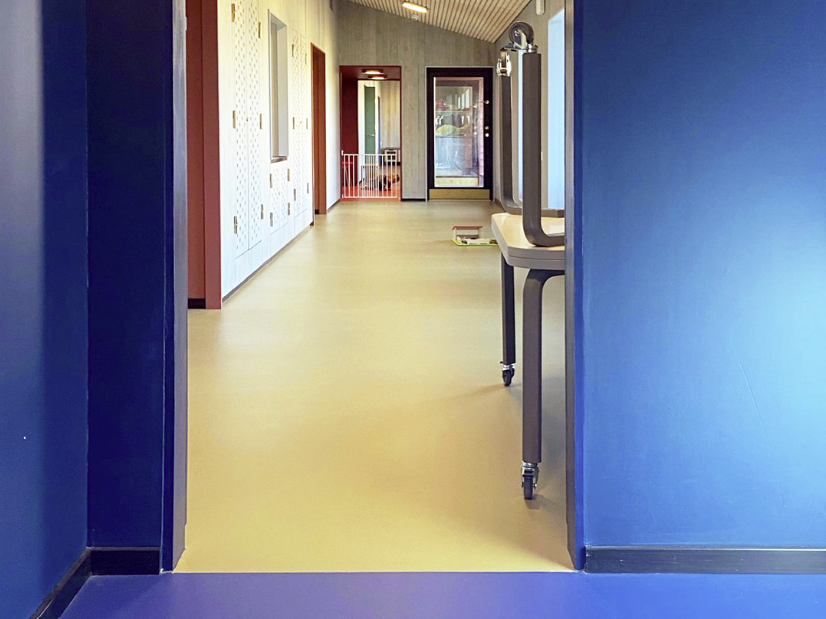 døråpning mellom to rom i en barnehage. Innerste rommet har blå vegger og gulv, det rommet vi ser inn i har lyse vegger og gulv