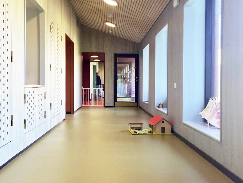 gangen i en barnehage med lyse vegger og gulv. Et lite lekehus står på gulvet til høyre foran vinduene