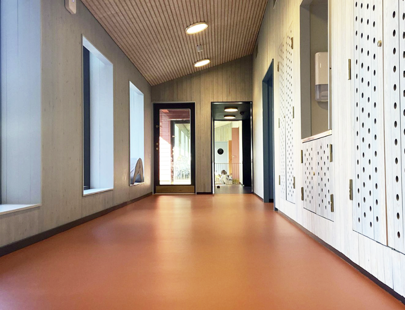 gangen i en barnehage med lyse vegger og rødlig gulv