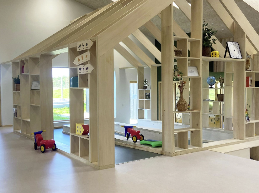 et lekerom i en barnehage bygget som et hus hvor veggene er hyller fyllt med leker og andre interiørartikler