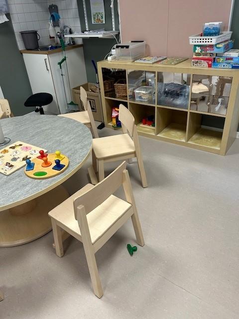 utsnitt av en liten sittegruppe for barn med stoler og bord. i bakgrunnen en hylle med leker