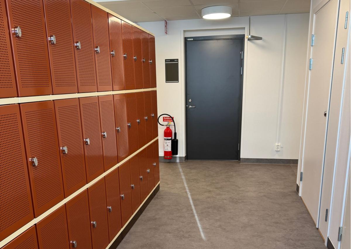 garderobe på en skole med rød garderobeskap til venstre og inngang til toalett til venstre. Midt i bildet ser du en dør