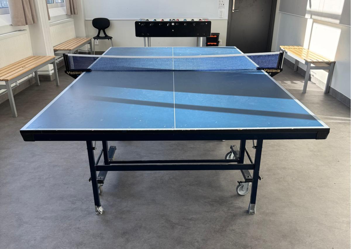 et bordtennisbor med blå bordplate i et klasserom på en skole. IPå veggen i bakkant er det en whiteboard tavle