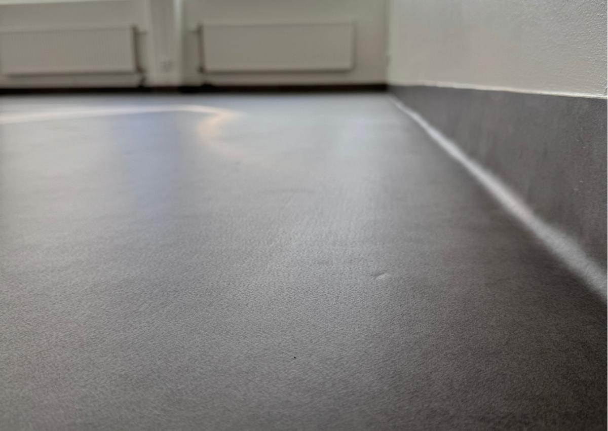 nærbilde av overgangen mellom gulv og vegg. Gulvet former en list noen cm opp på veggen