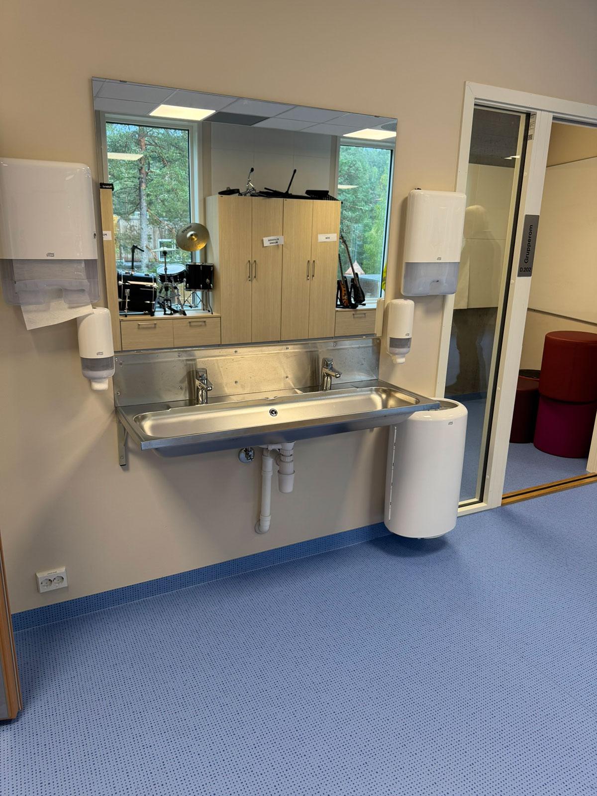 En bred vask med speil over plassert på veggen i fellesområdet på en skole