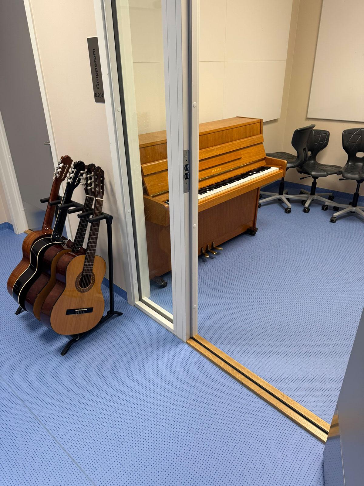 Åpningen inn til et rom hvor det står et piano. På utsiden av rommet ved siden av døren til venstre står det et stativ med fire gitarer