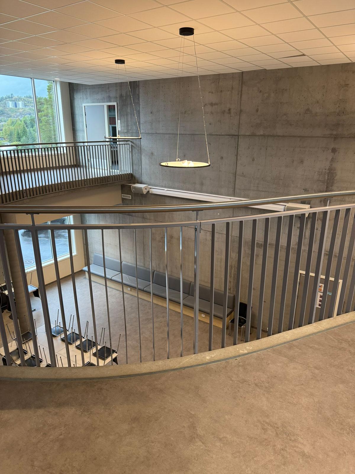 Fellesområde på en skole med betongvegger og grått gulv. I midten kan man se ned til etasjen under gjennom sprinklene i et rekkverk