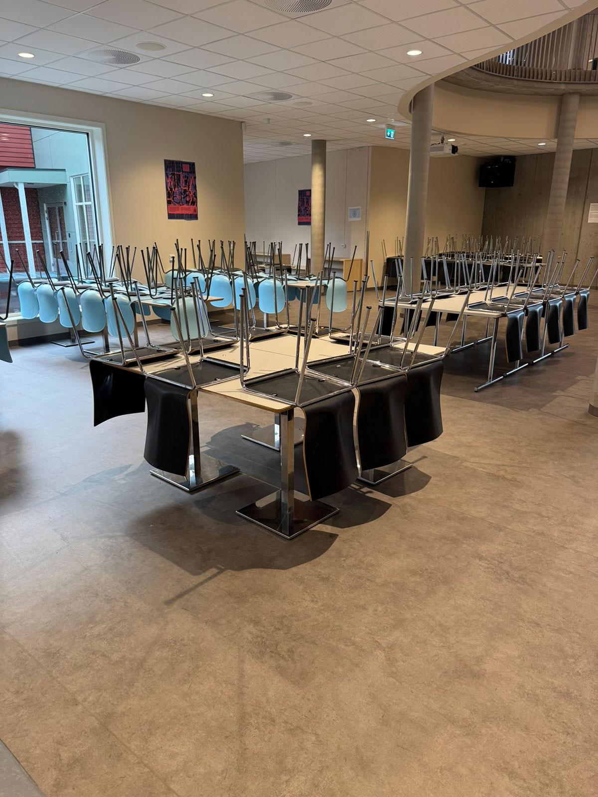 Felles oppholdssted på en skole med bord og stoler i grupper. Stolene er vendt opp ned og står oppå bordene