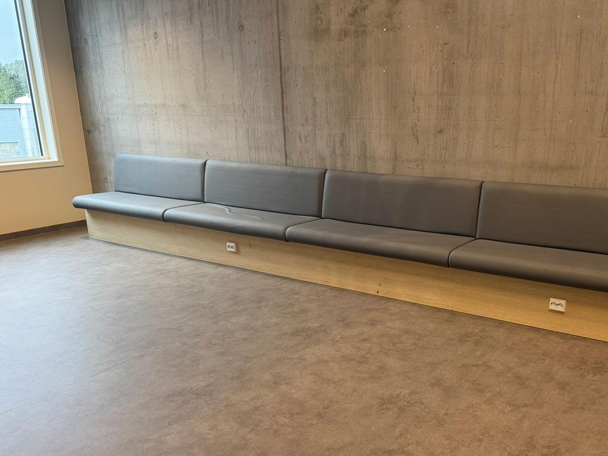 en lang benk med grått skinn stående inntil en betongvegg i fellesområde på en skole