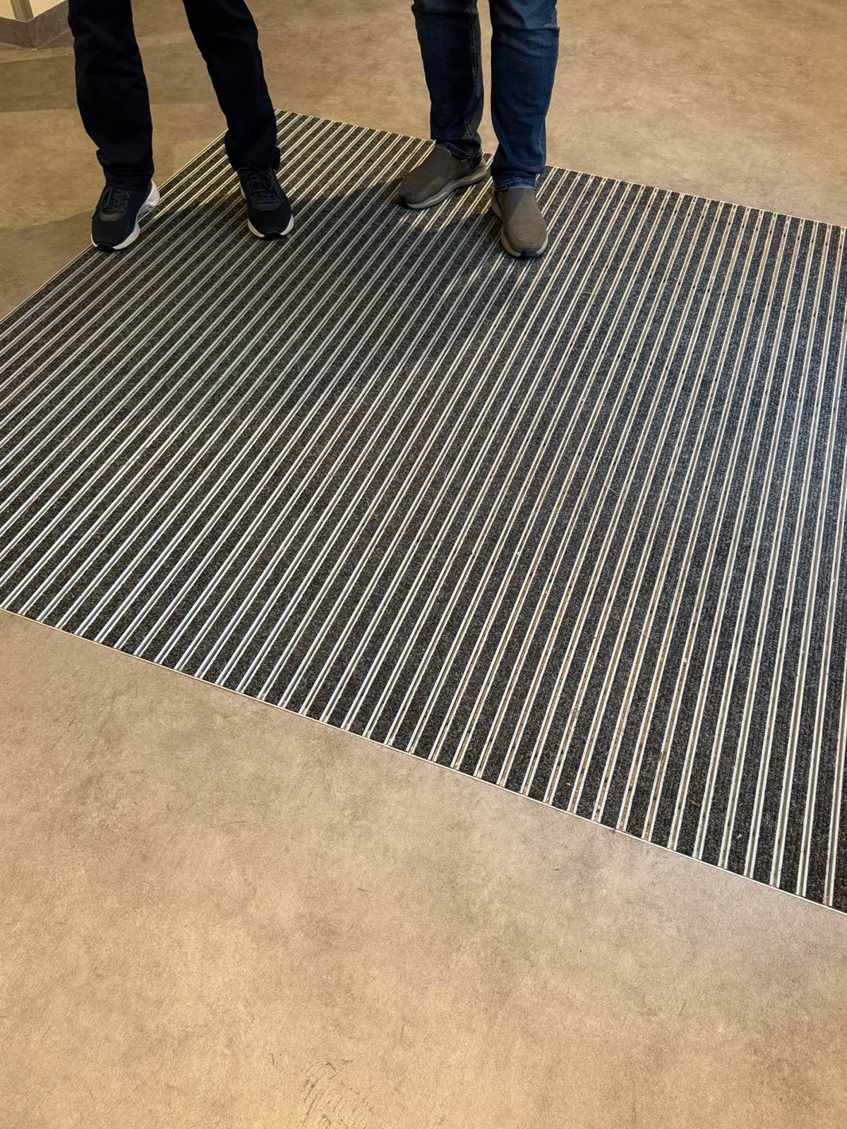 benene til to personer som står på en matte innenfor en inngangsdør.