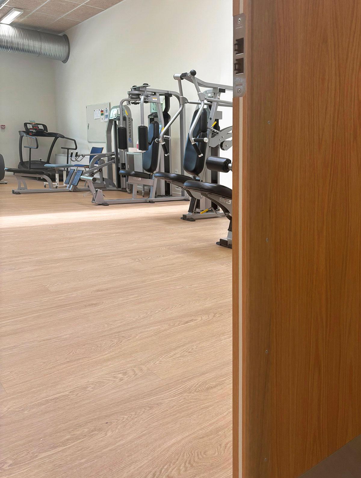 et treningsrom med treningsapparater. man kan så vidt se deler av den åpne døren til høyre i bildet