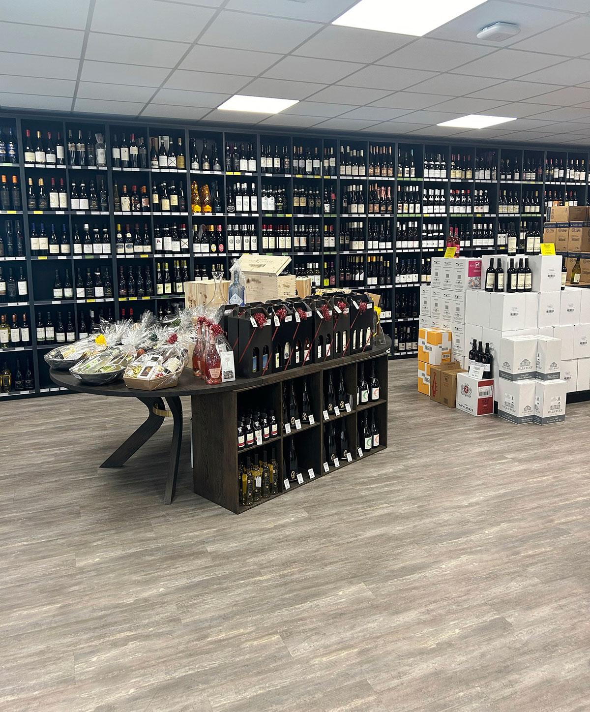 butikk med hyller langs hele bakveggen med vin. I forgrunnen ser man et butikktorg og til høyre noen vinesker med løse  flasker stående oppå