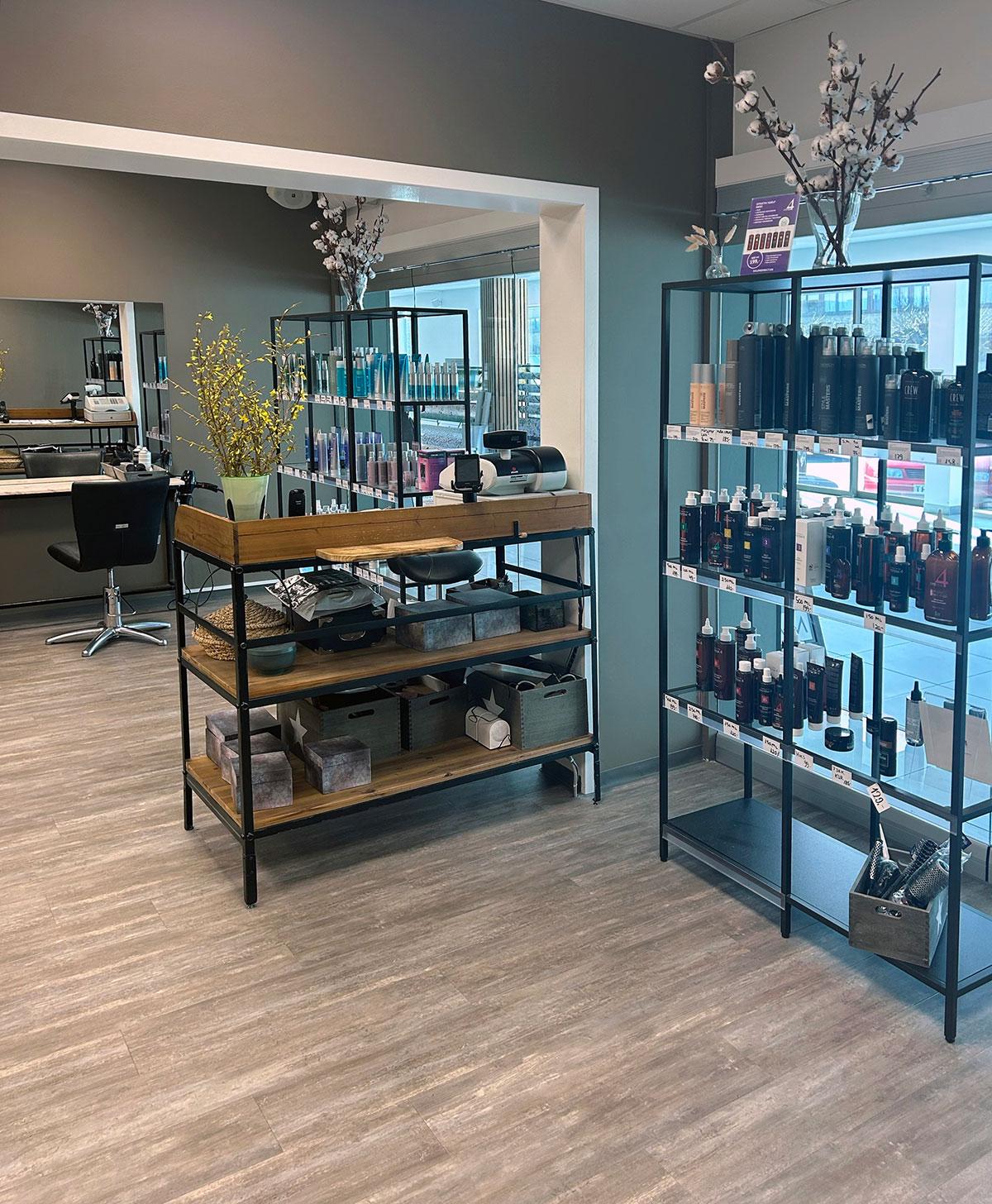 en frisørsalong hvor man ser hyller med varer foran et vindu til høyre og en tom frisørstol foran et speil innerst i rommet