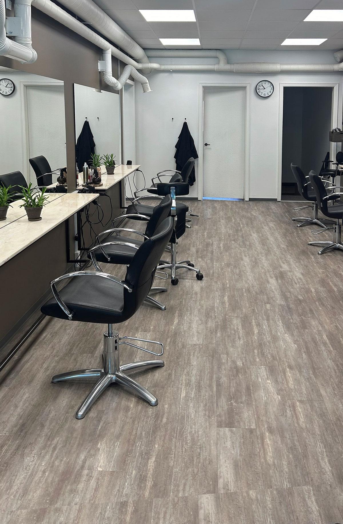 en rekke med tomme frisørstoler stående foran et langt speil på veggen til venstre