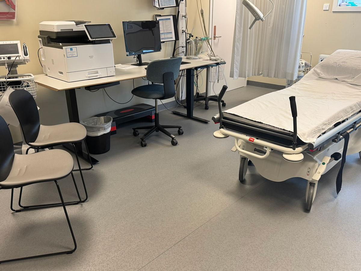 et behandlingsrom med seng til høre, stoler til venstre og skrivebord med pc og printer i midten