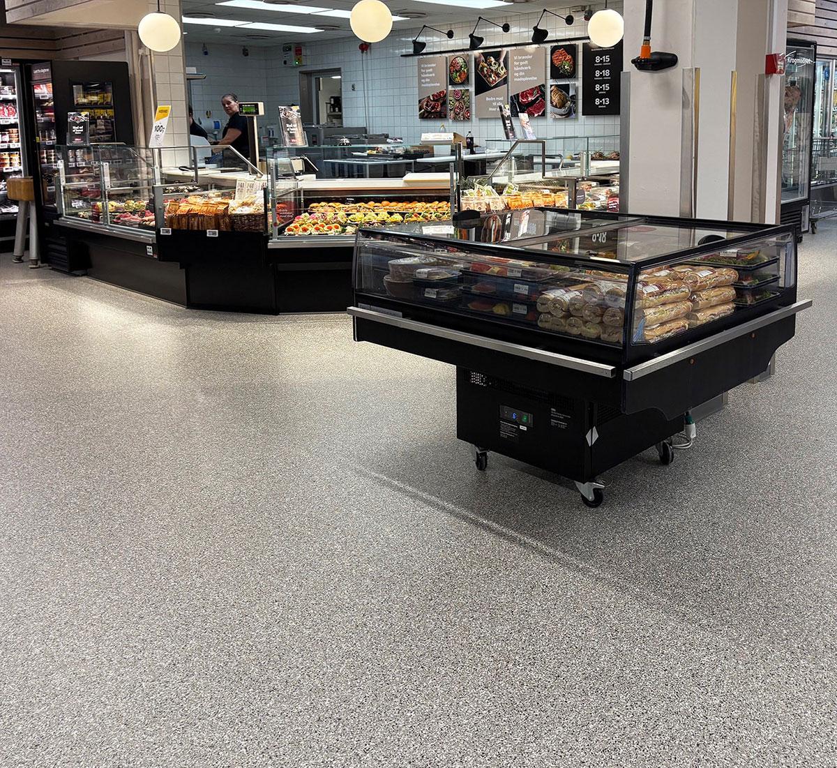 en kjøledisk med hjul stående midt på gulvet foran ferskvaredisken i en butikk