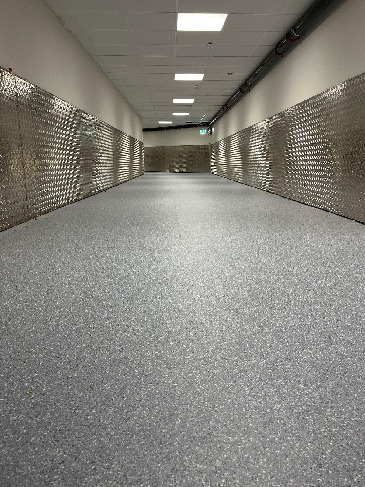 en lang gang på et sykehus med grått gulv og beskyttelsesplater på veggene