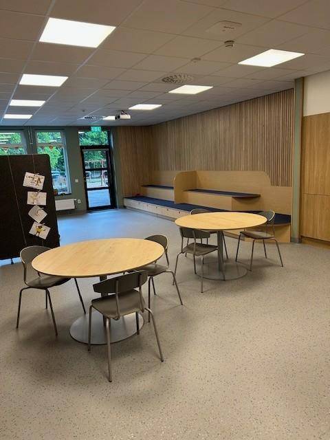 fellesrom på en skole med runde bord med stoler rundt.