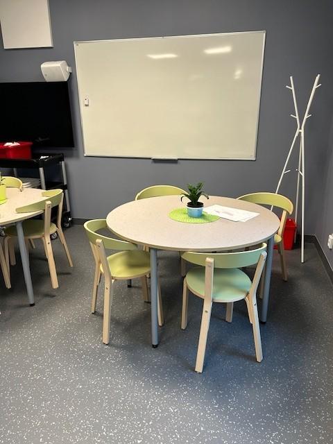 et klasserom på en skole med runde bord og stoler. Tavle/whiteboard hengende på veggen