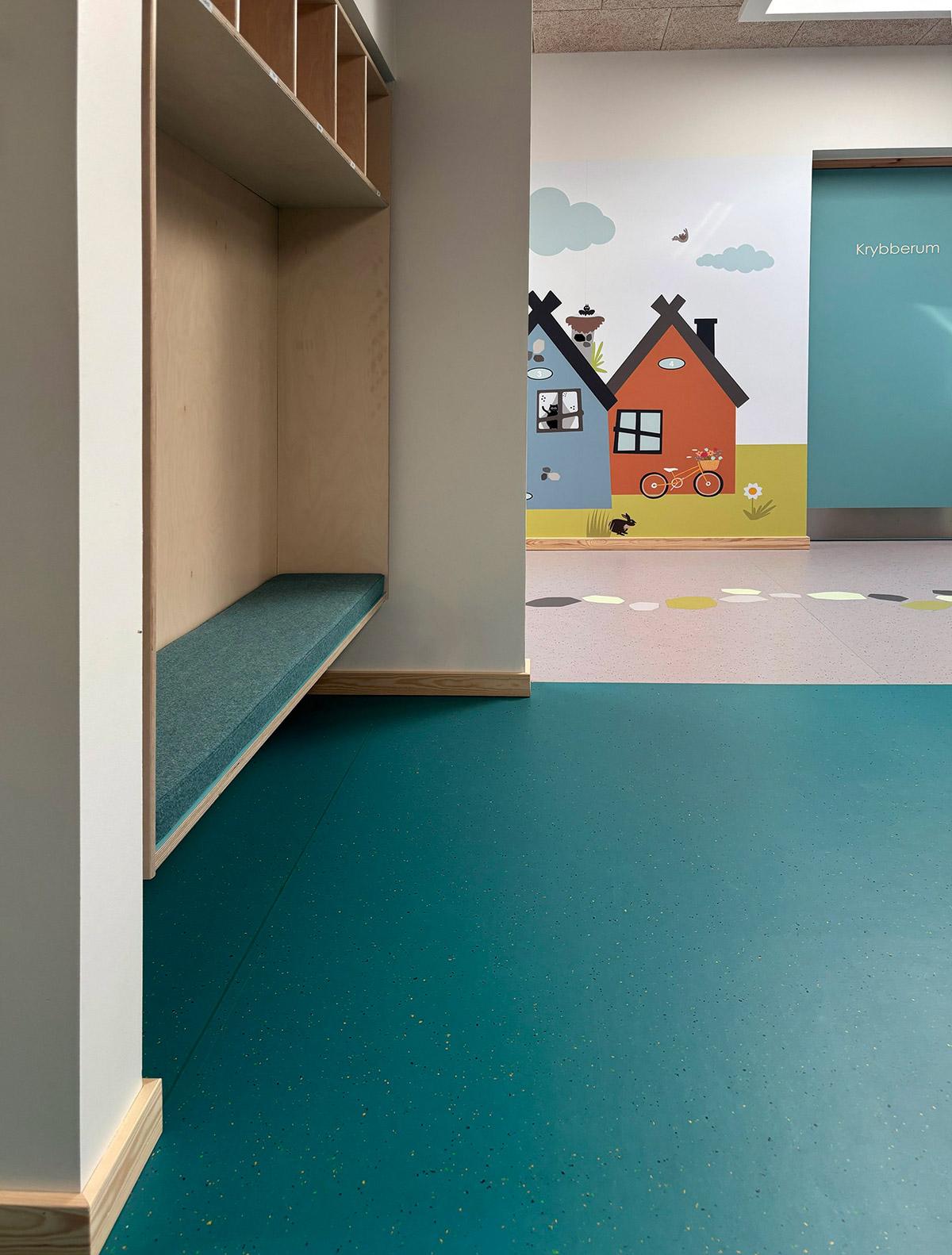 garderobe i en barnehage med blått gulv. i bakgrunnen ser man ut i gangen