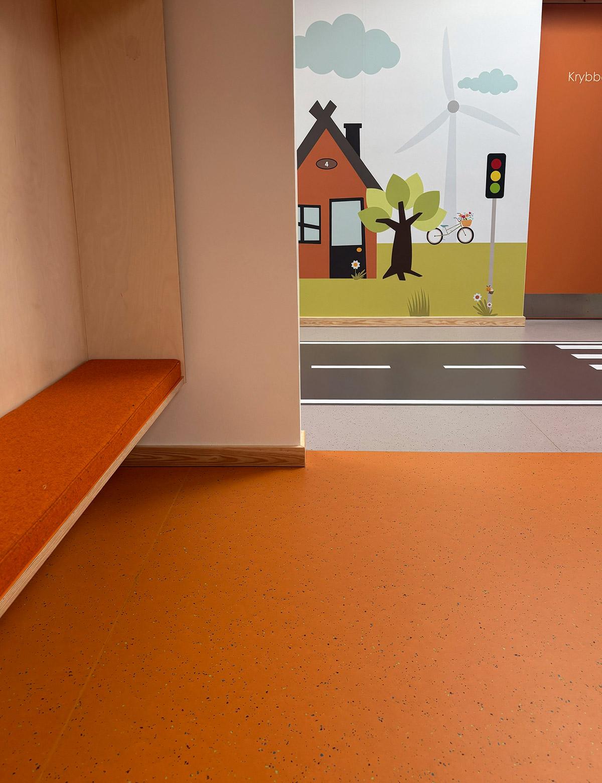 garderobe i en barnehage med orange gulv. i bakgrunnen ser man ut i gangen