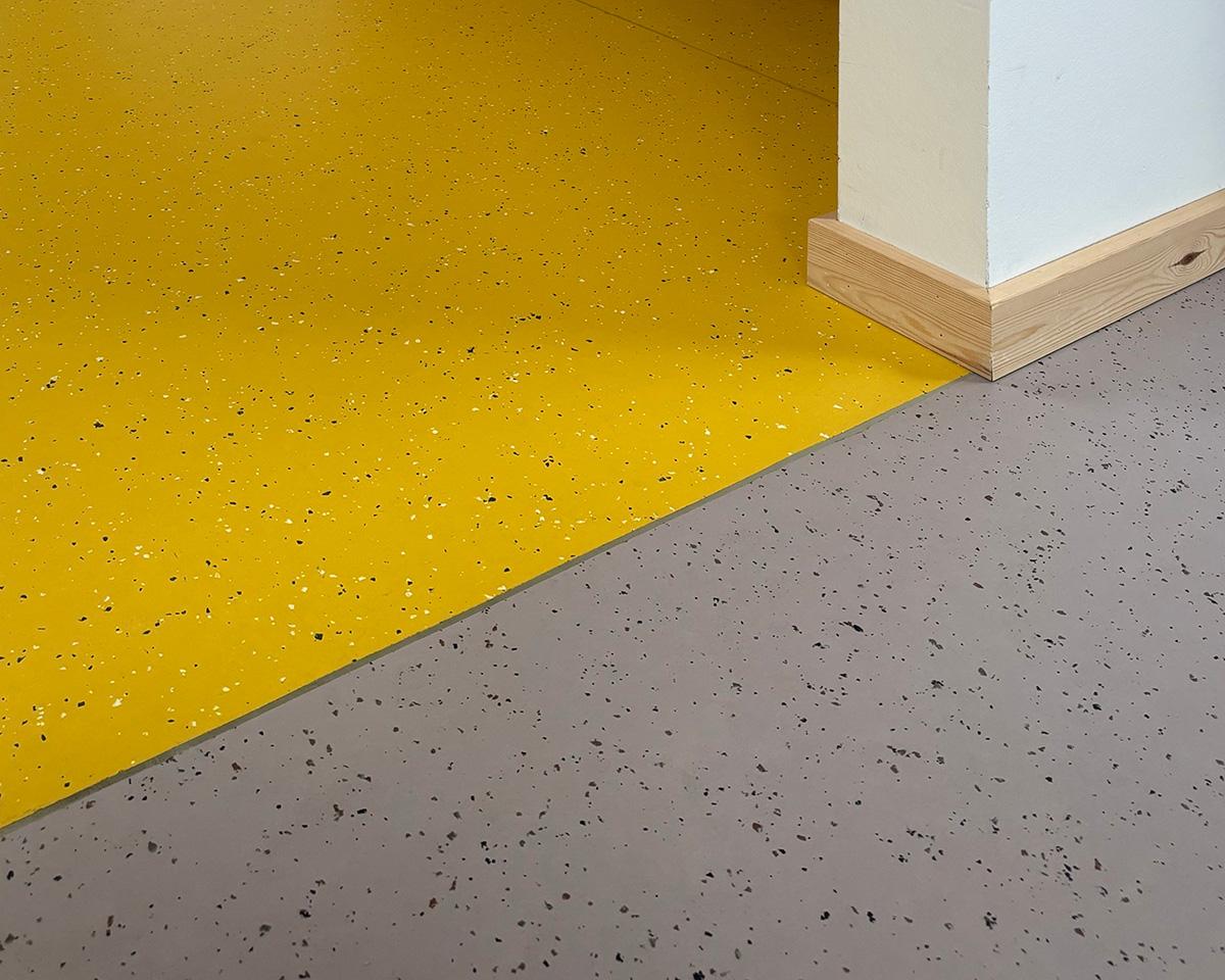 skille mellom to soner i en barnehage. grått gulv nederst og gult gulv i øverst i bildet