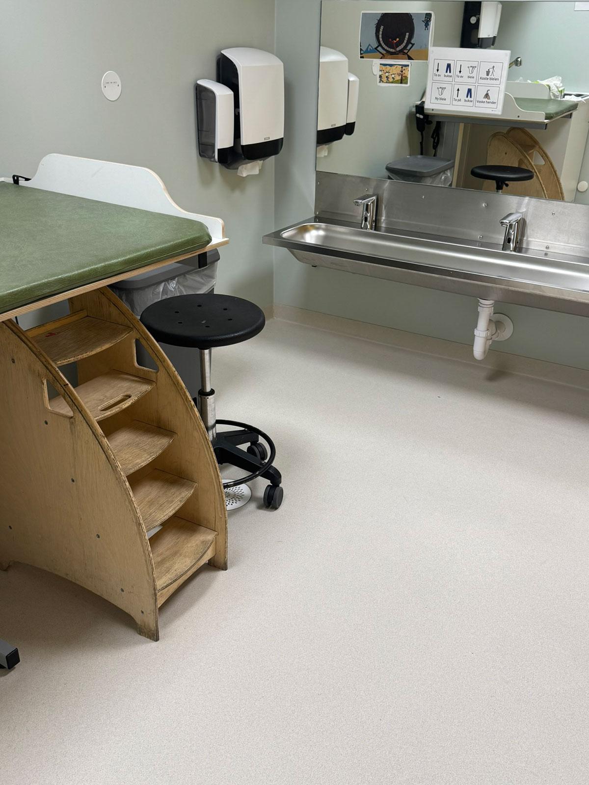 Eet våtrom med lang vask tilpasset barn i bakgrunnen. Til venstre en behandlingsbenk med liten trapp opp