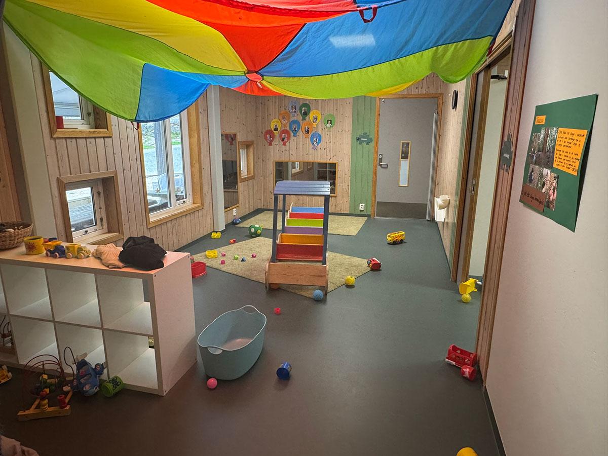 Lekerom i en barnehage med hyller og skap, leker strødd utover gulvet og et fargerikt seil festet i taket